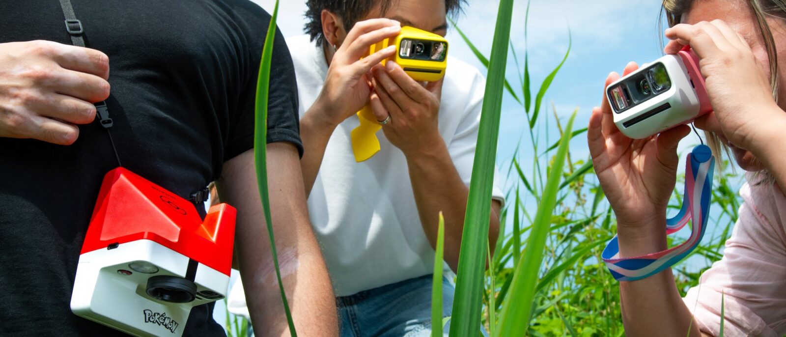 Trois amis photographient dans les herbes hautes avec les appareils Polaroid x Pokémon aux couleurs de Pikachu, de Nymphali et de la Poké Ball